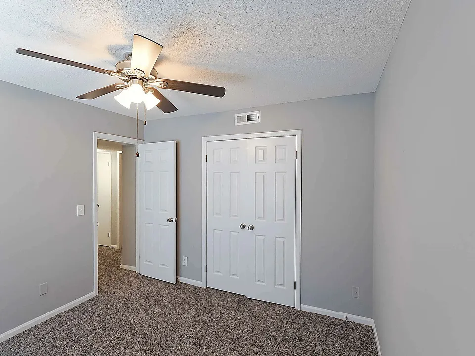 Spacious bedroom with plush carpeting, ceiling fan, and natural light