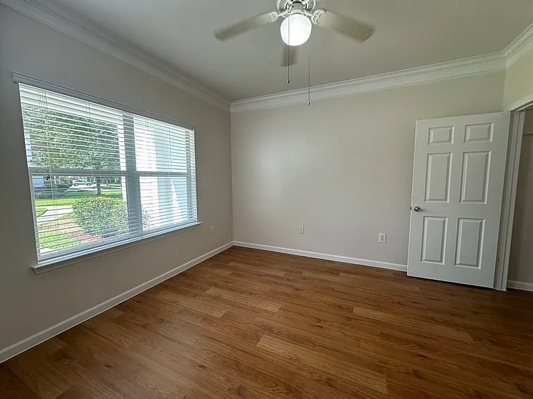Bright, inviting bedroom with large window, wood-style floors, and modern ceiling fan. Bright, inviting bedroom with large window, wood-style floors, and modern ceiling fan.