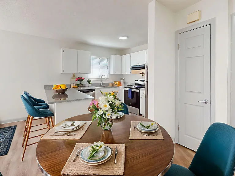 Bright and inviting open-concept kitchen and dining area featuring modern appliances, elegant teal chairs, and a cozy round table set for a delightful dining experience.