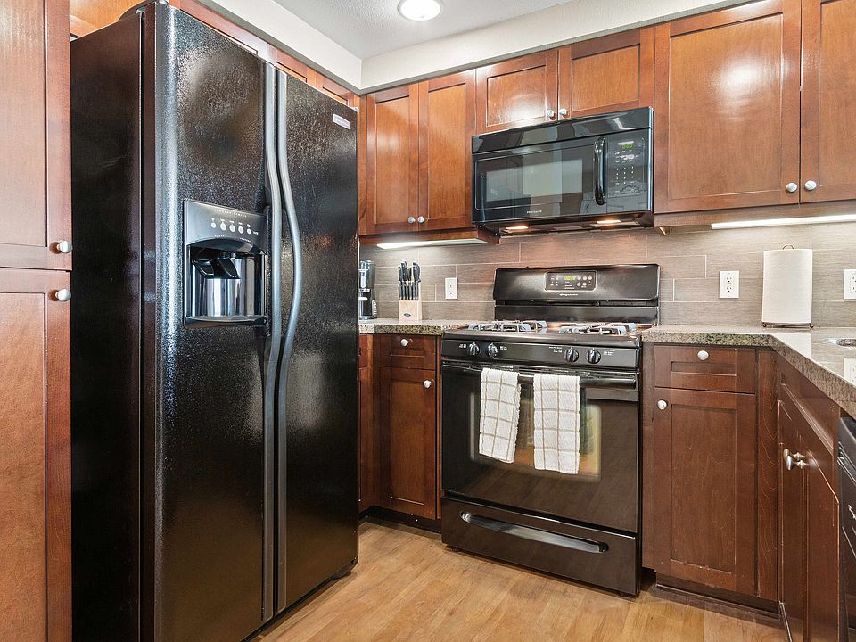 Modern kitchen with black appliances, wood cabinetry, and granite countertops.
