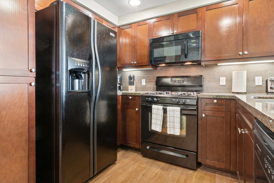 Modern kitchen with black appliances, wood cabinetry, and granite countertops.