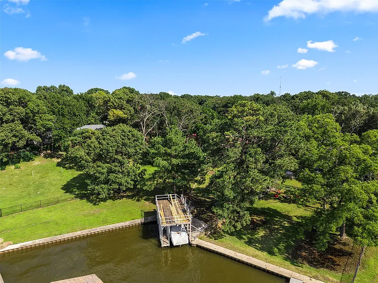 Waterfront property featuring a private boat dock, concrete retaining wall, and expansive green lawn