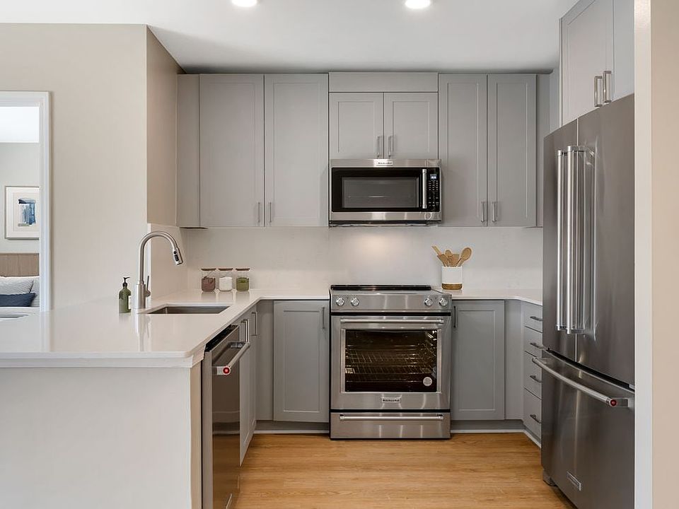 Signature Collection kitchen with grey cabinetry, white marbled quartz countertops and backsplash, stainless steel appliances, and hard surface flooring
