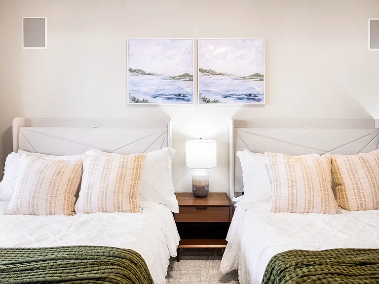 Two beds with wingback storage headboard,crisp white linens,cozy pillows and blankets,symmetrical bedside tables with chic lamps, and an artistic accent wall.