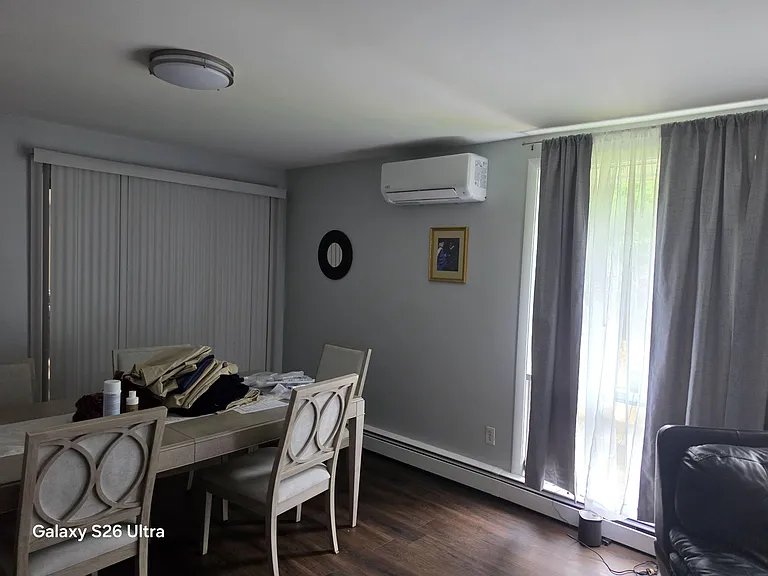 Dining area with a full-size table, large window treatments for privacy, and a wall-mounted mini-split for comfort.
