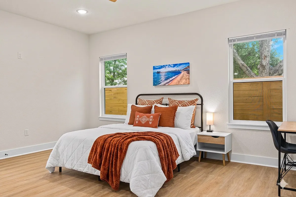 Well-appointed bedroom with a full bed, two windows, bedside table, and a dedicated desk area for work or study. - Carle Ave
