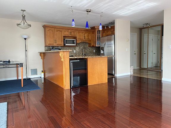 Open kitchen with an electric stove, dishwasher, microwave, fridge, and wine cooler. Front door by the sliding mirrors. Stacked washer-dryer behind the mirror.