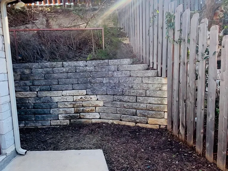 Private backyard with stacked stone retaining wall and concrete patio