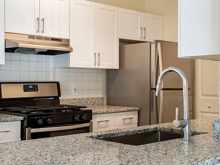Renovated Package I kitchen with white cabinetry, grey speckled granite countertops, white tile backsplash, stainless steel appliances and hard surface plank flooring throughout common areas