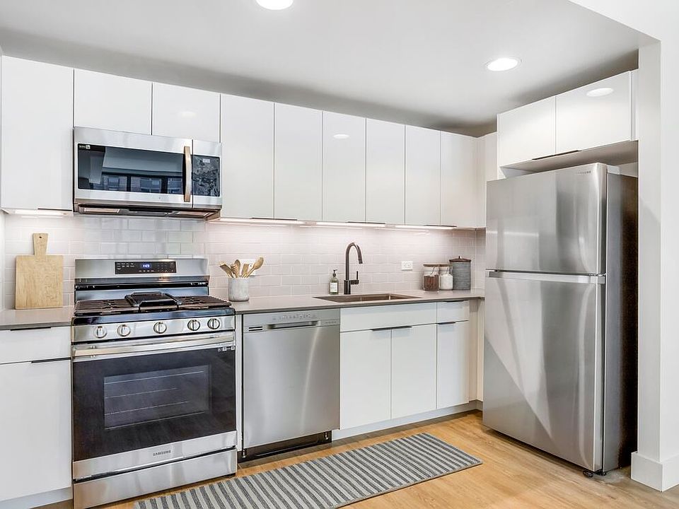 Renovated Package I kitchen with grey quartz countertops, white cabinetry, light grey tile backsplash, stainless steel appliances, and hard surface flooring