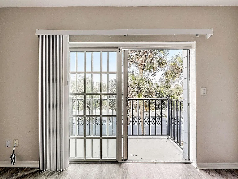 Bright and airy room with sliding glass doors opening to a charming balcony overlooking lush palm trees.