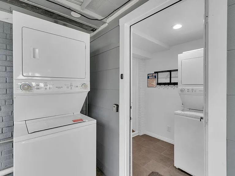 Dedicated laundry area with stacked washer and dryer units, durable tile flooring, and wall-mounted hooks for easy storage.
