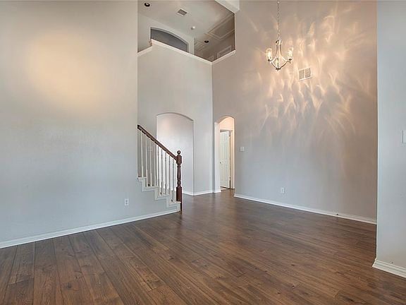 Empty room with arched walkways, stairway, dark wood-style floors, a chandelier, and a towering ceiling