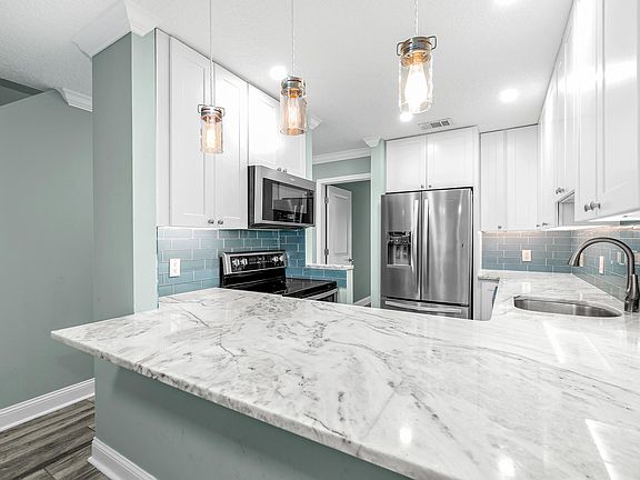 Kitchen with marble countertops and stainless steel appliances. Edison bulb pendant lights and under the counter lights. All on dimmers.