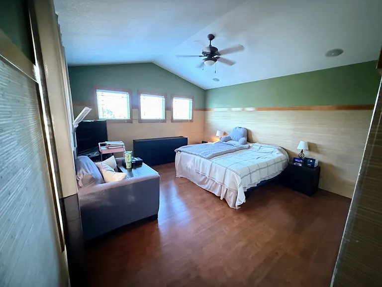 Primary bedroom, many windows, vaulted ceiling, grass wallpaper, walk in closet, ceiling fan, no carpet, and private bath.