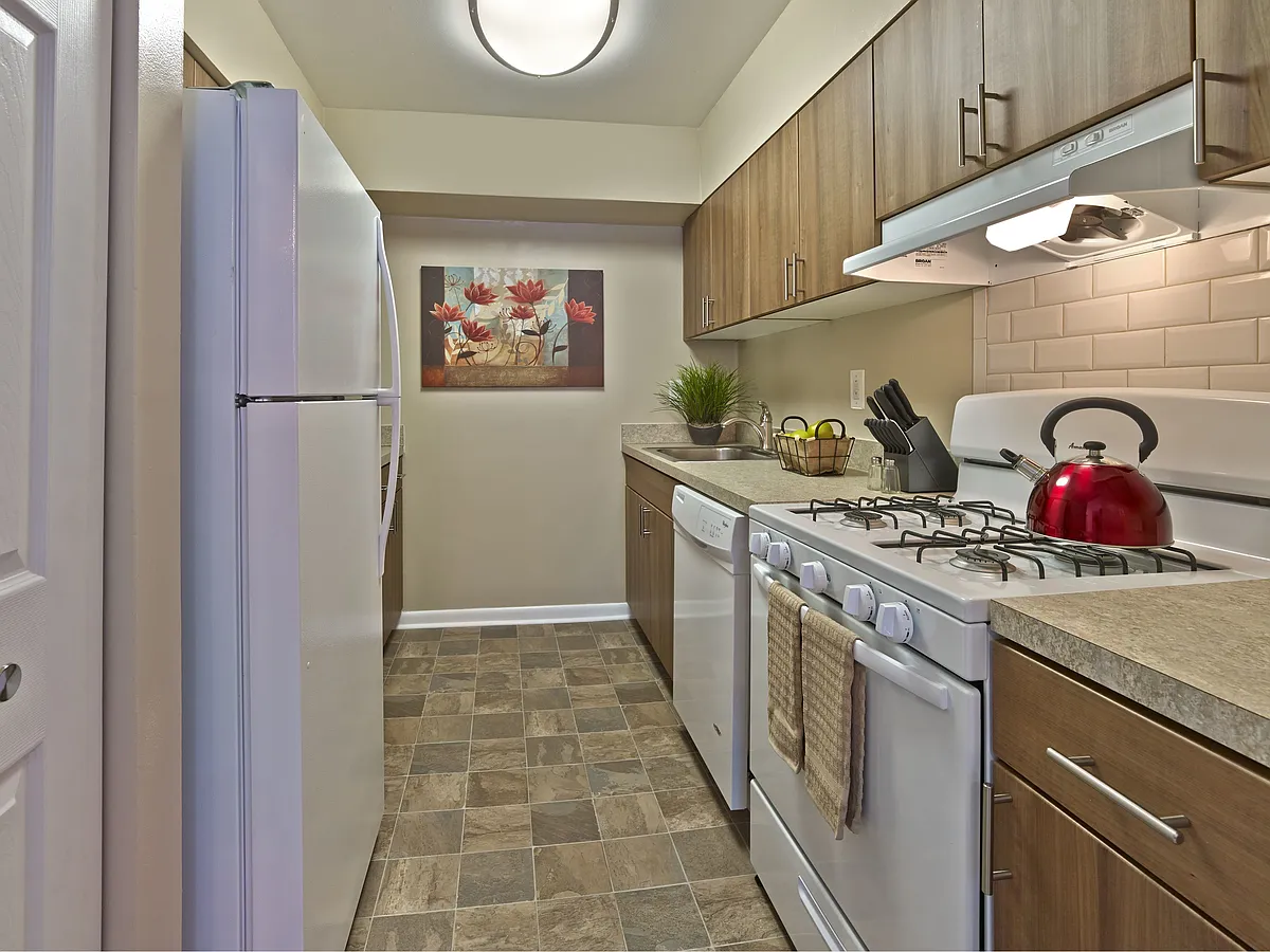 Stylish renovated kitchen at Haynes Run Apartments featuring wood cabinetry, gas cooking, a tile backsplash, and updated countertops for a modern living experience. - Haynes Run