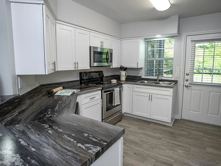 Sleek black fusion countertops, abundant white shaker cabinetry, and stainless-steel appliances create an elegant and functional culinary haven in this spacious kitchen with a breakfast bar.