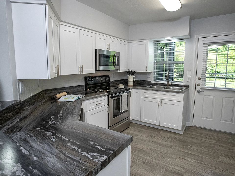 Sleek black fusion countertops, abundant white shaker cabinetry, and stainless-steel appliances create an elegant and functional culinary haven in this spacious kitchen with a breakfast bar.