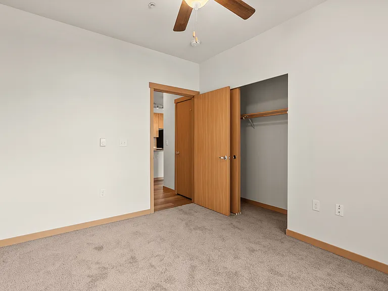 Bright and cozy bedroom with plush carpet, ceiling fan, open closet space, and wooden accents. Bright and cozy bedroom with plush carpet, ceiling fan, open closet space, and wooden accents.