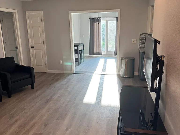 Open living area with wood-look flooring, mounted TV setup, and easy flow to the dining space with sliding glass doors.