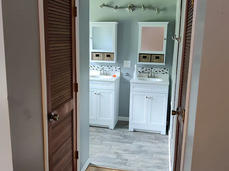 Master bedroom's bathroom as viewed from master bedroom, walk way to bathroom has a walk in closet on each side with custom wood floor. Bathroom has custom tilework, 2 vanities, walk in shower area with corner seat and tub.