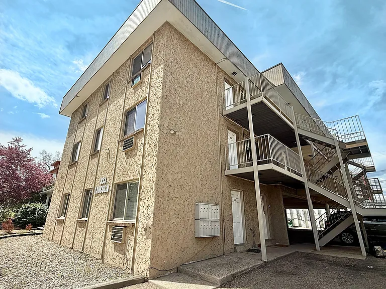 Charming three-story apartment building with modern staircases and textured exterior under a clear blue sky.