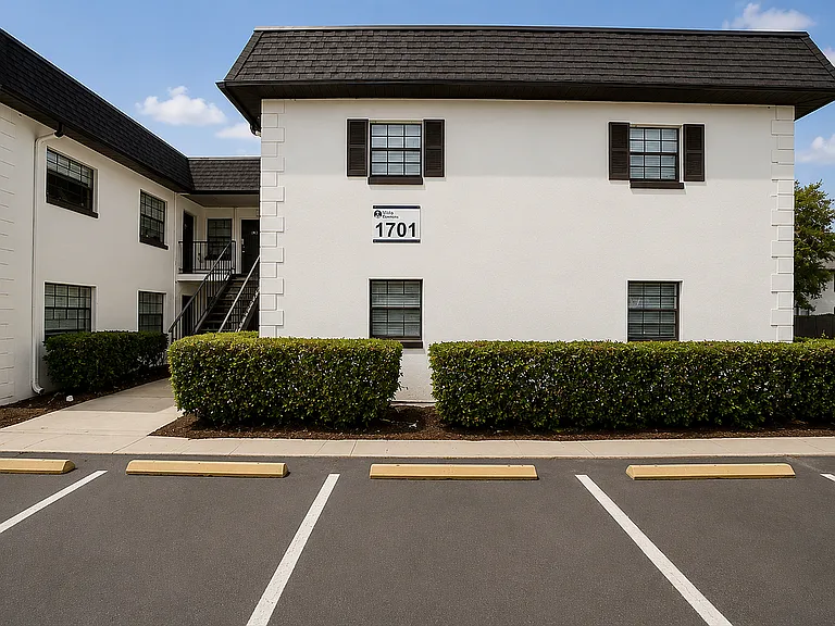 Charming white two-story apartment building with lush greenery, spacious parking, and serene surroundings.