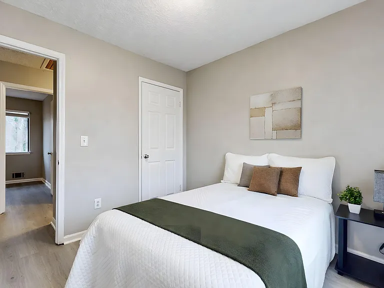 Furnished bedroom with a full-size bed, neutral finishes, and an adjoining hallway for easy access to shared spaces.
