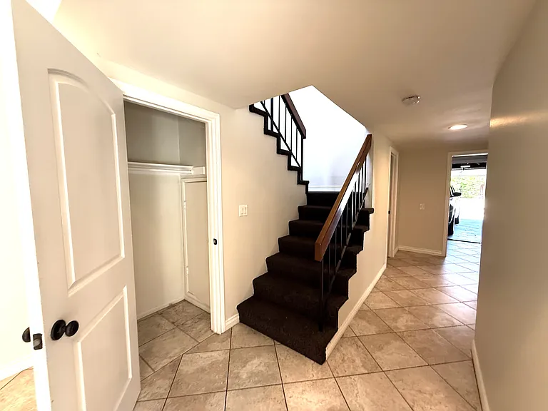 Stairs leading to upstairs primary bedroom suite. Storage sloset at bottom of stairs. Hall leading to 3 car garage.