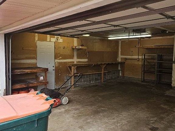 Left side of garage with suspended storage shelf, metal shelving and 2 work benches.