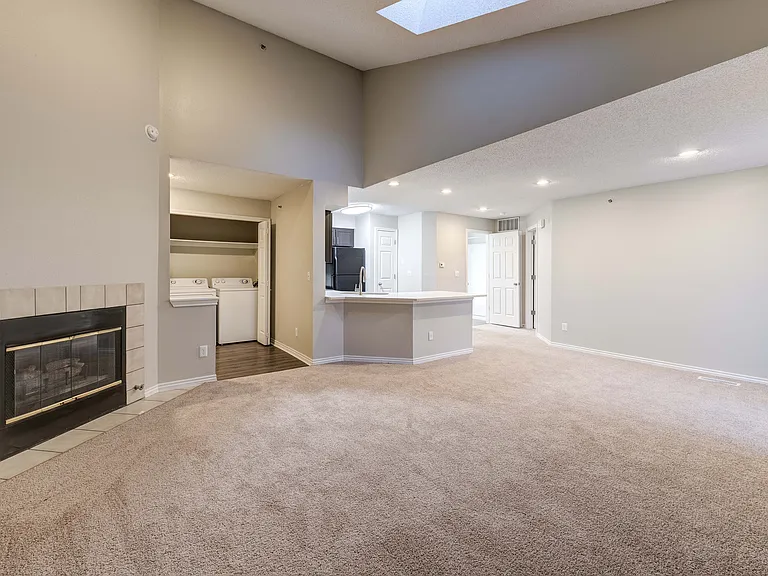 Bright open-plan living area with plush carpet, cozy fireplace, modern kitchen, and in-unit laundry alcove.