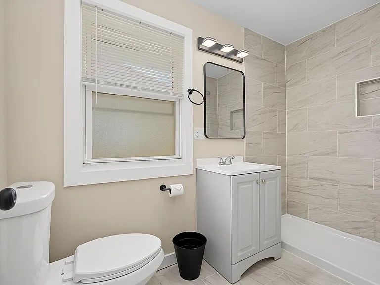 Updated bathroom with a tiled tub/shower surround, vanity with storage, and a window with blinds for ventilation.