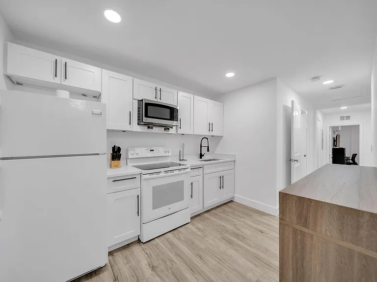 Galley kitchen with ample white cabinetry, full appliance package, and a long island for prep space and casual seating.