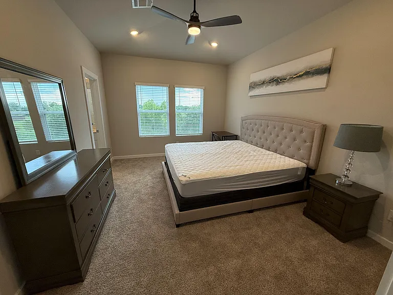 Well-sized bedroom with two large windows, ceiling fan, and a full furniture set including bed, nightstand, and dresser.