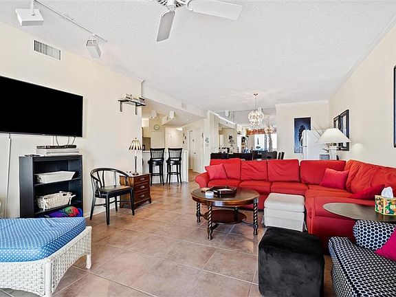 Living room featuring rail lighting, ceiling fan with notable chandelier, ornamental molding, and light tile patterned floors