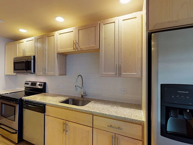 Apartment kitchen with granite countertops and wood-style flooring.