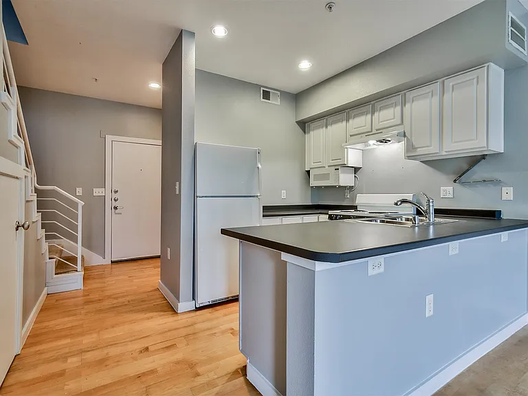 Kitchen area featuring light gray cabinetry, dark countertops, a stainless steel sink, and white appliances