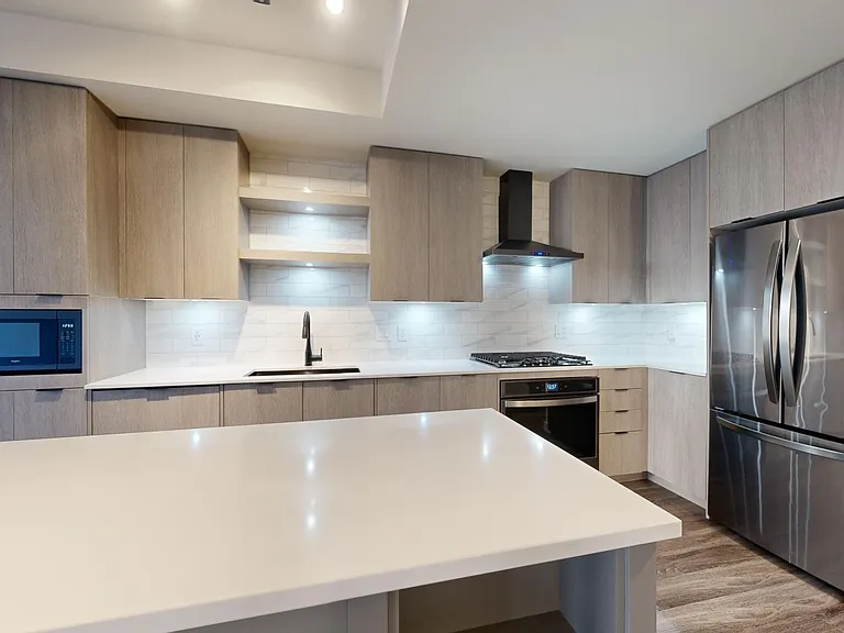 Apartment kitchen with black stainless steel appliances, quartz countertops, wood-style flooring, and custom Italian cabinetry.
