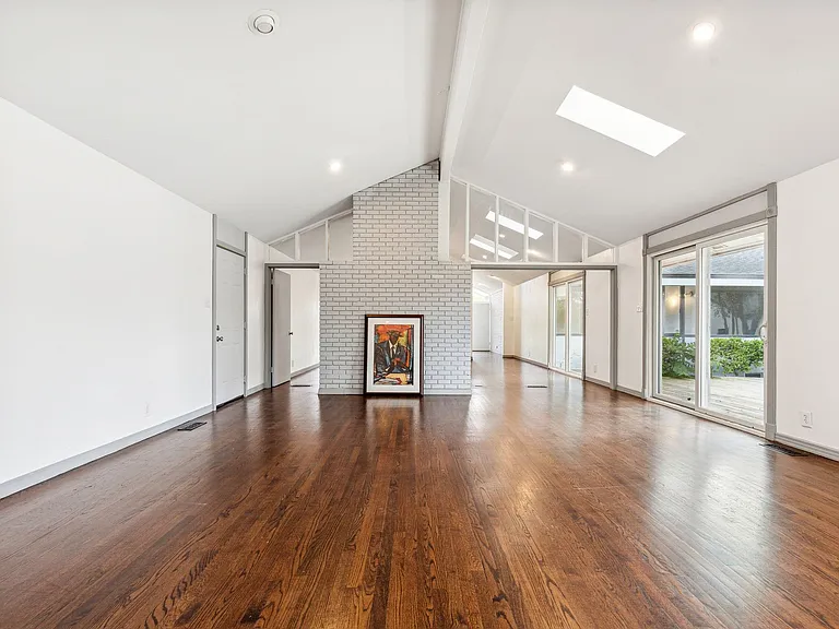 Spacious living area featuring wood-finish flooring, a vaulted ceiling with skylights, and a painted brick fireplace