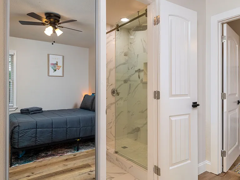Relax in a modern, spa-style bathroom with a marble-tiled walk-in shower, sleek black fixtures, bright vanity lighting, and clean finishes. Directly connected to the primary bedroom for privacy and convenience.