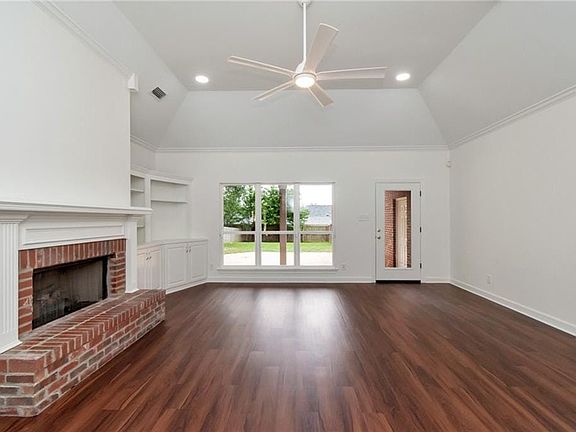 Unfurnished living room with dark wood-style flooring, a brick fireplace, ceiling fan, visible vents, and baseboards