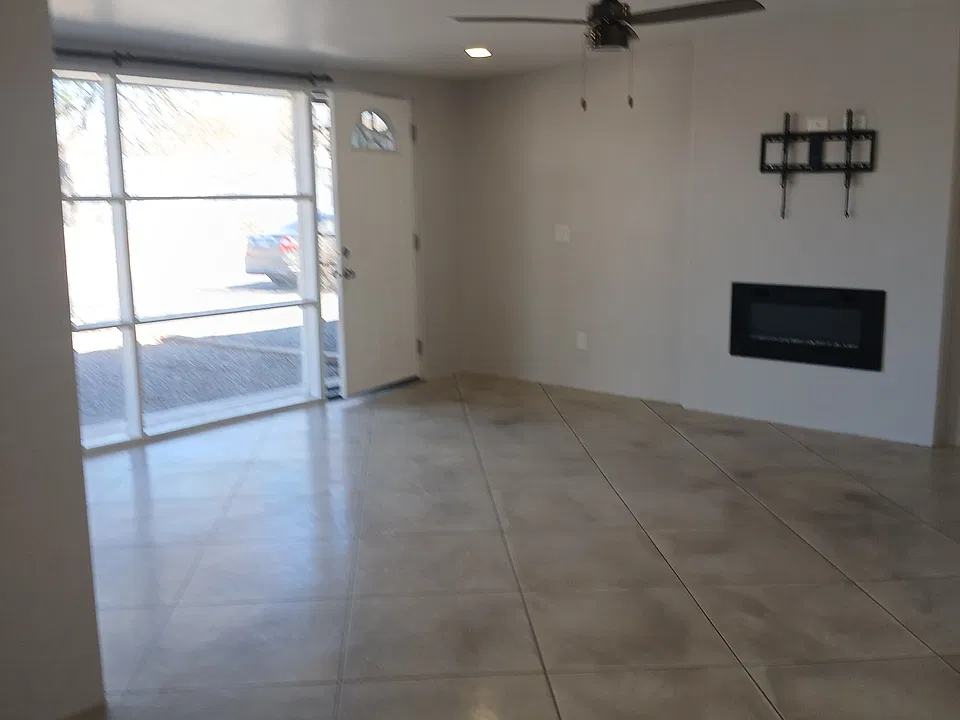 View from the dining room into the living room showing the front door and the large floor ceiling window and also the LED fireplace.