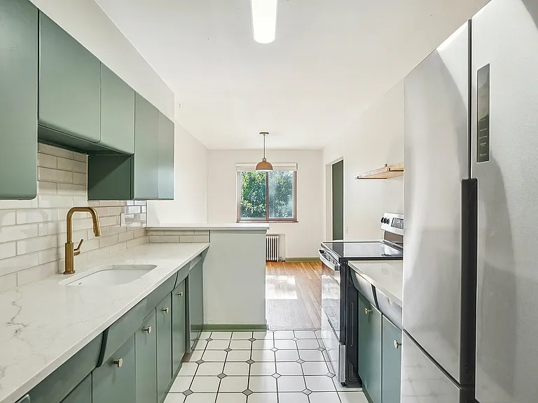 Modern apartment kitchen with sleek green cabinets, marble countertops, and stainless steel appliances, featuring a large window for natural light.