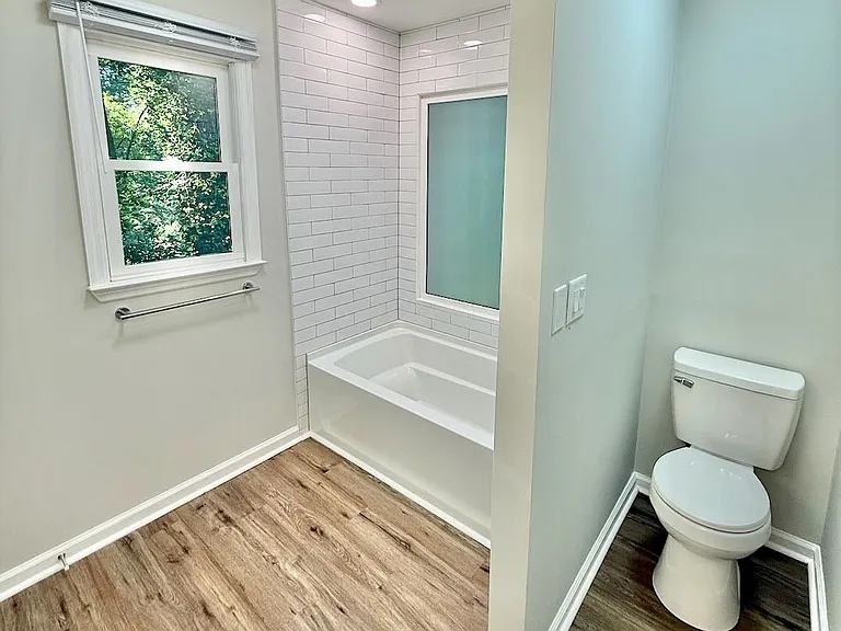 Bright serene bathroom retreat_ - new floor-to-ceiling subway tile and frosted window fill the space with light - wood-look LVP floors and deep soaking tub invite you to unwind in comfort every day.