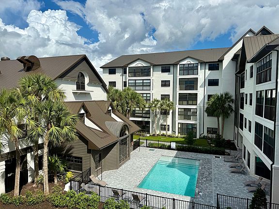 Inviting apartment complex with a serene swimming pool, surrounded by lush palm trees and modern architecture under a vibrant sky.