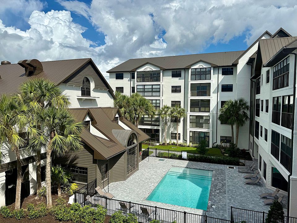 Inviting apartment complex with a serene swimming pool, surrounded by lush palm trees and modern architecture under a vibrant sky.
