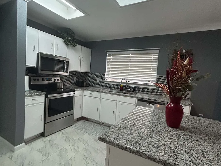 Spacious kitchen with granite-look counters, ample white cabinetry, mosaic tile backsplash, and stainless steel appliances.