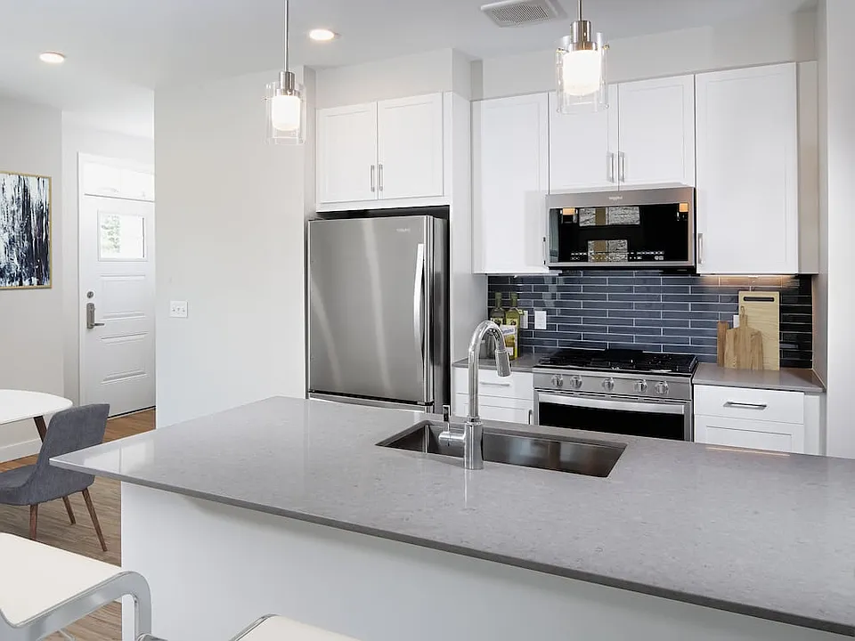 Phase II Renovated Package I apartment kitchen with stainless steel appliances, grey quartz countertops, white cabinetry, dark grey tile backsplash, and hard surface flooring