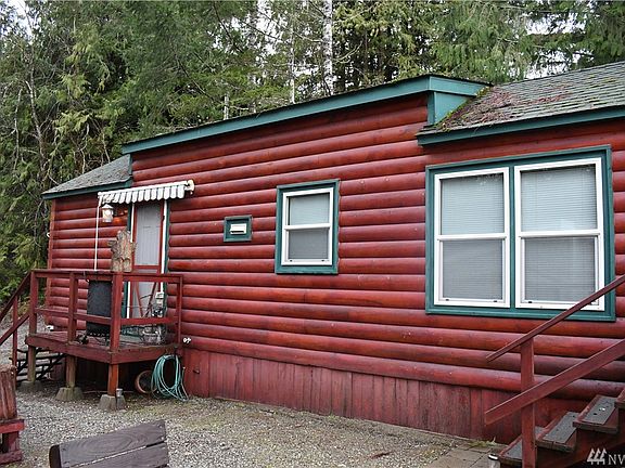 Side view. With stairs leading to main entrance and covered back deck area. Low maintenance gravel between home and woodshed.
