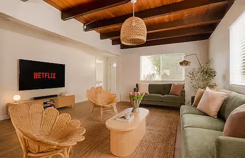 Bright and welcoming living room with comfy sofas, stylish rattan chairs, and a wooden coffee table stocked with board games. Perfect mood for game nights, cozy Netflix binges, or lounging on an air mattress.